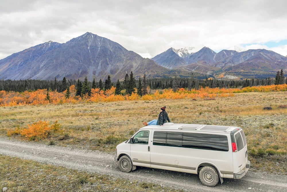 sitting on top of a diy camper van conversion in front of the mountains