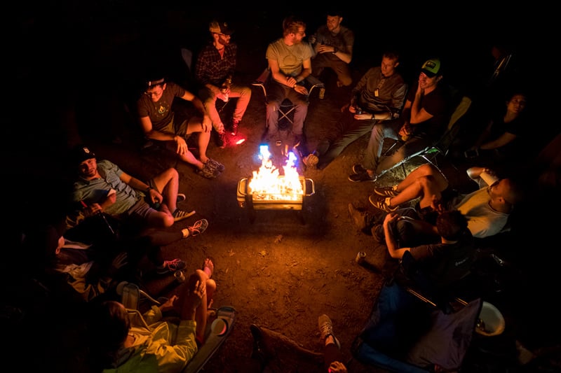 group of friends sitting around a portable campfire at a camping site