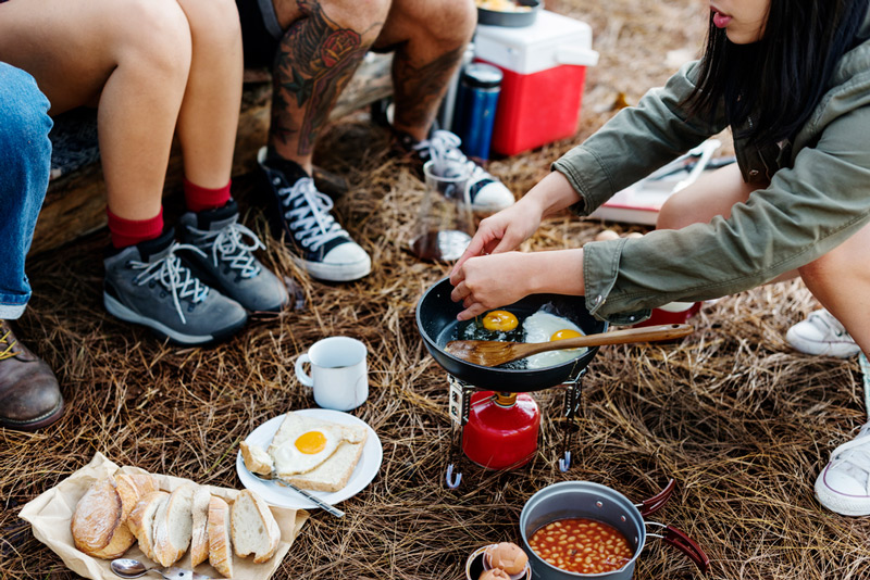 friends cooking over a campfire with cold food from a portable ice maker