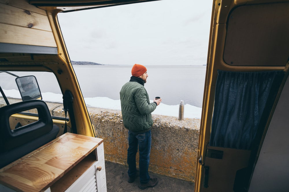 man drinking a cup of coffee outside of a camper van conversion