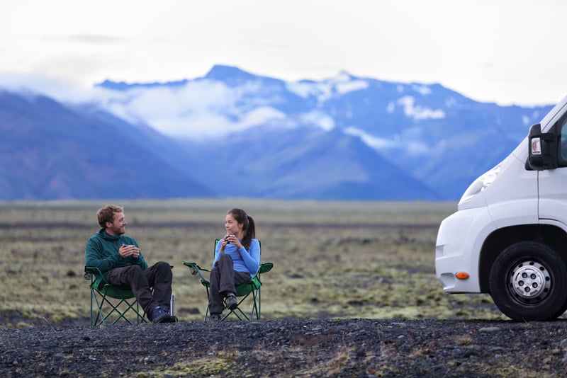 couple sharing a cup of coffee outside of their motorhome or travel trailer in the mountains