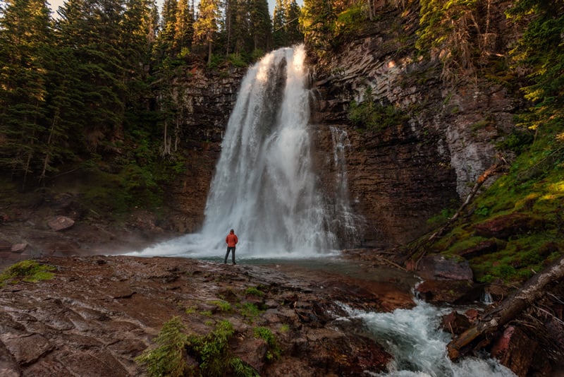 hiker standing next to virginia falls in glacier national park montana